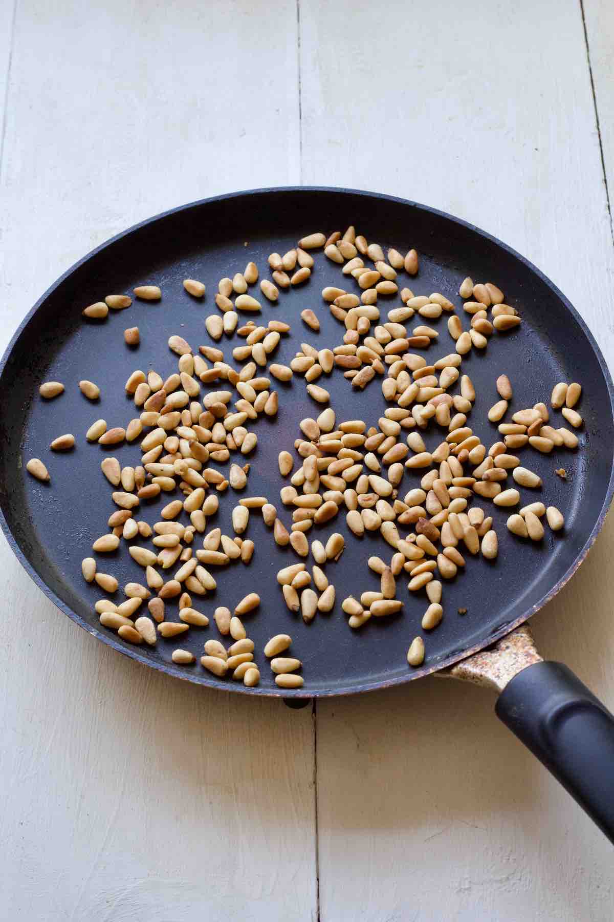 Toasted pine nuts in a frying pan.
