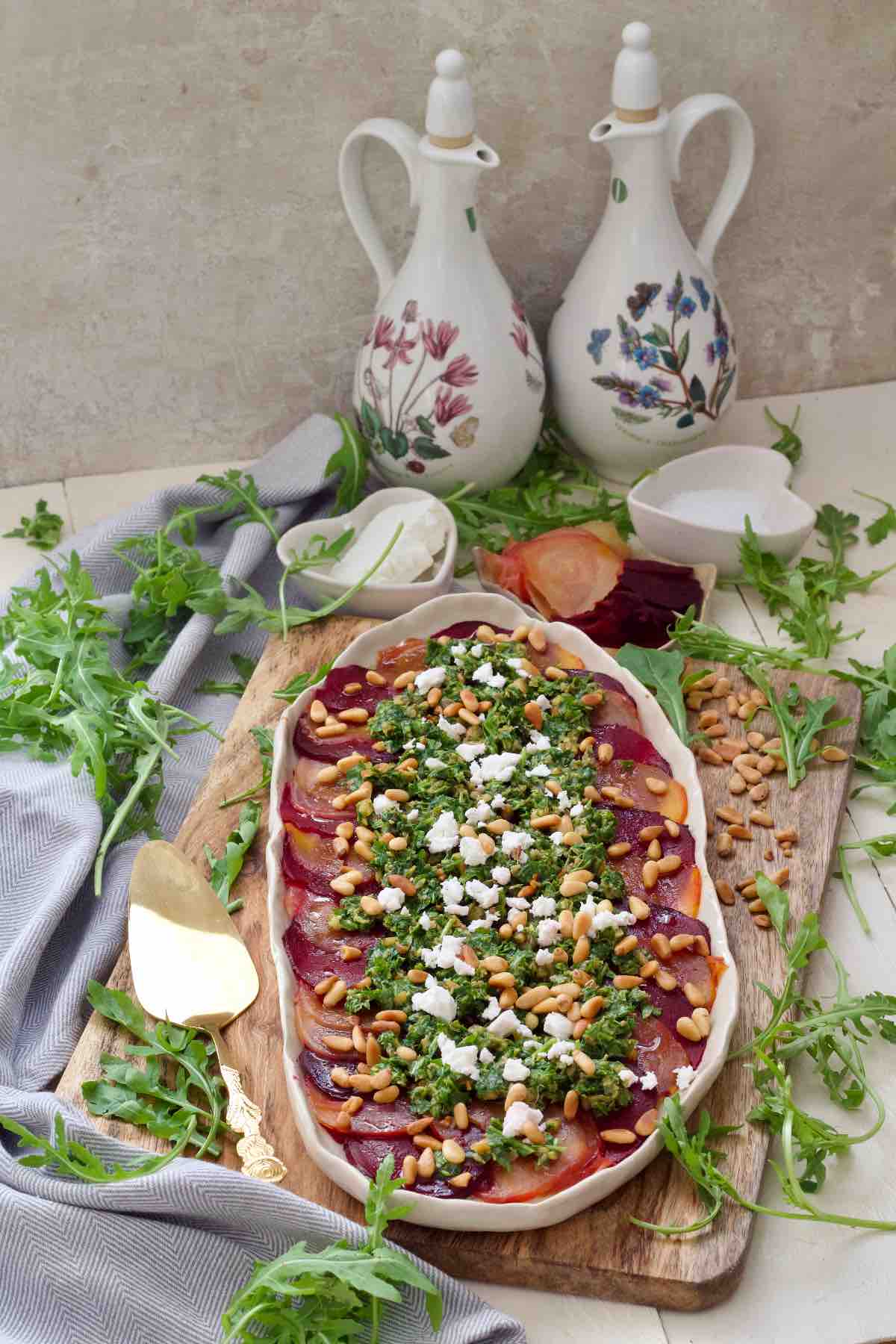 Bird view of beetroot carpaccio on a platter, rocket leaves around, two bottles at the back.