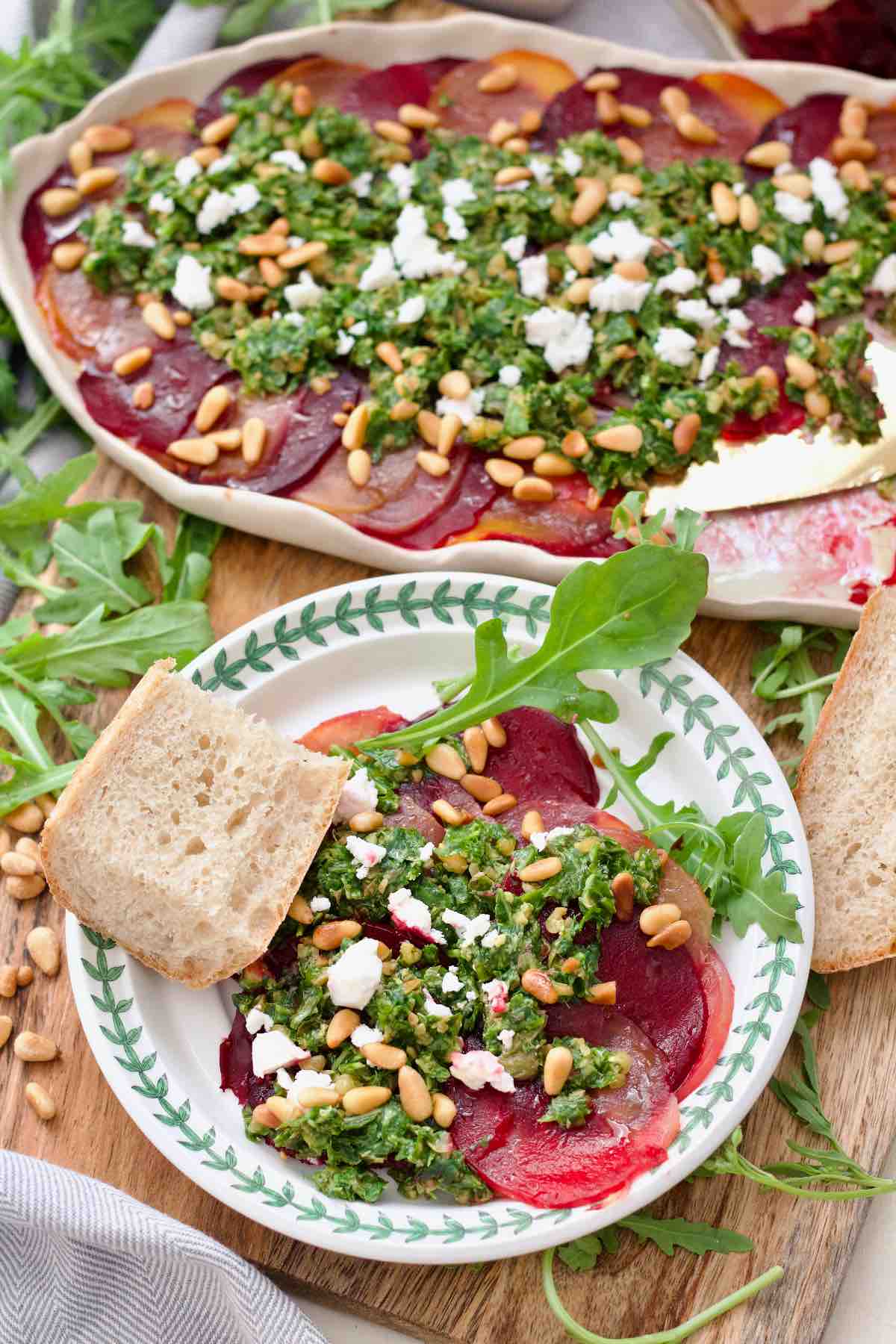 Plated portion of beetroot carpaccio with rocket salsa on a plate with a piece of bread.