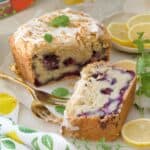 Close up of slice of cake and end of loaf cake with forks and lemon slices.