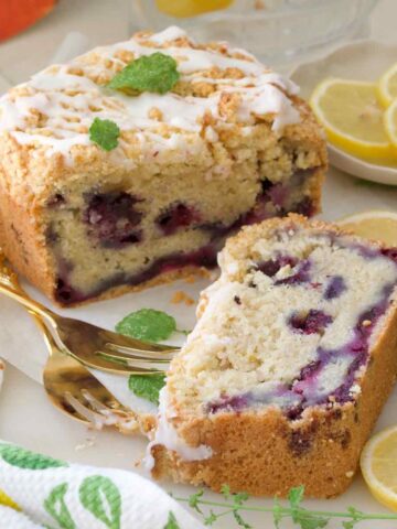 Close up of slice of cake and end of loaf cake with forks and lemon slices.
