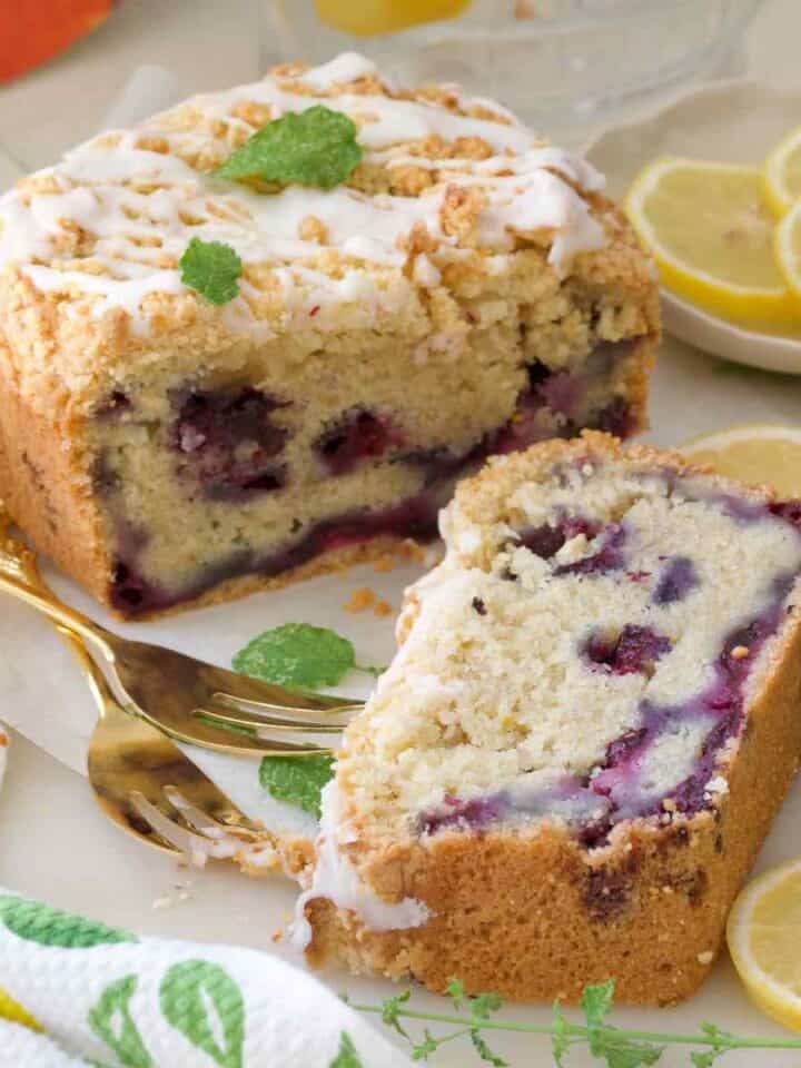 Close up of slice of cake and end of loaf cake with forks and lemon slices.