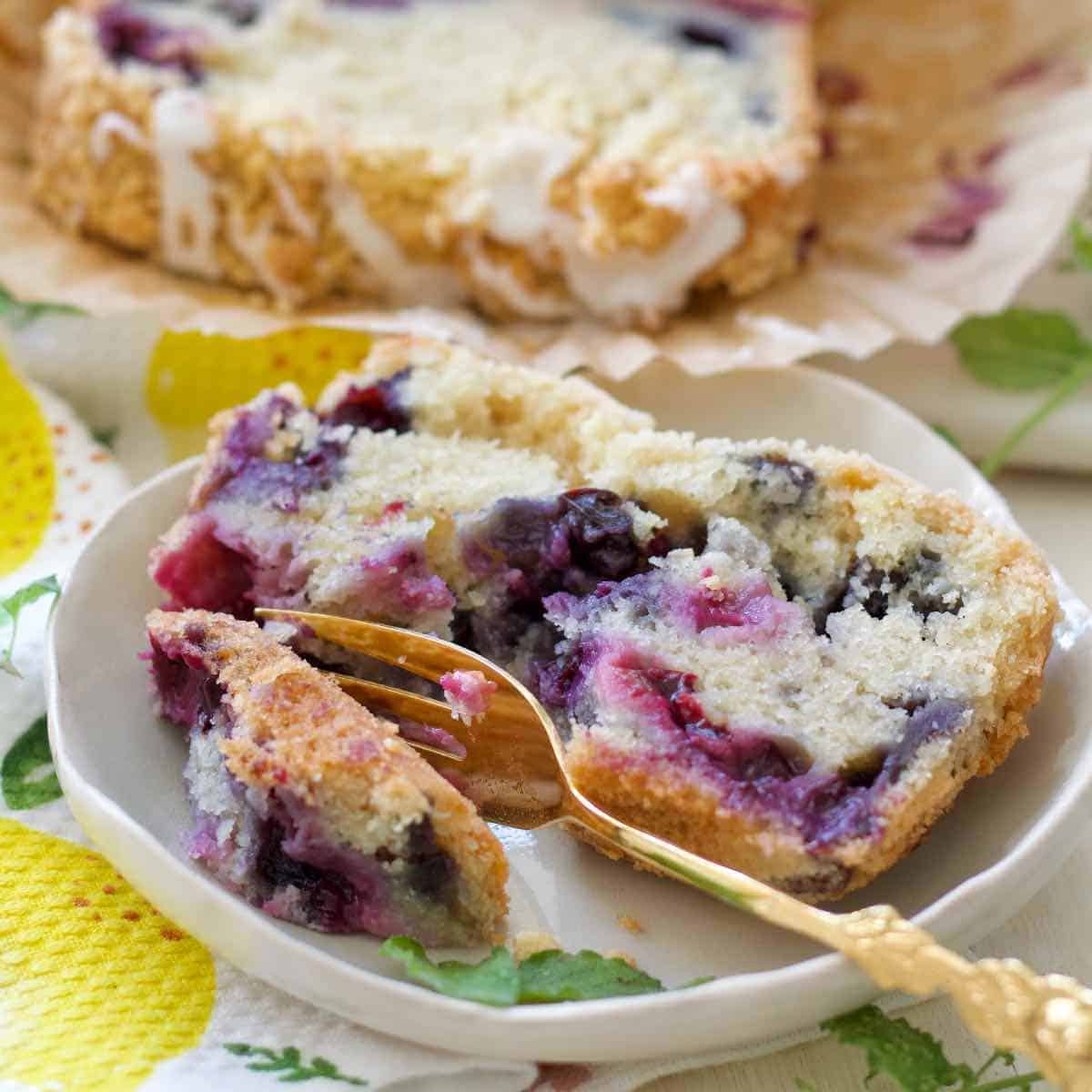 Close up of lemon and blueberry loaf cake slice on a plate with a fork.