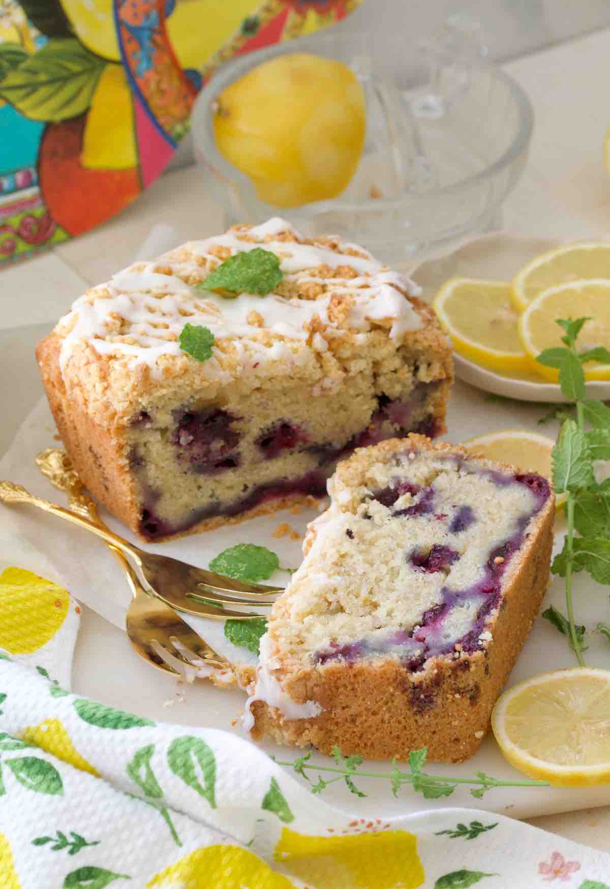 Slice of cake and end of loaf cake with forks and lemon slices.