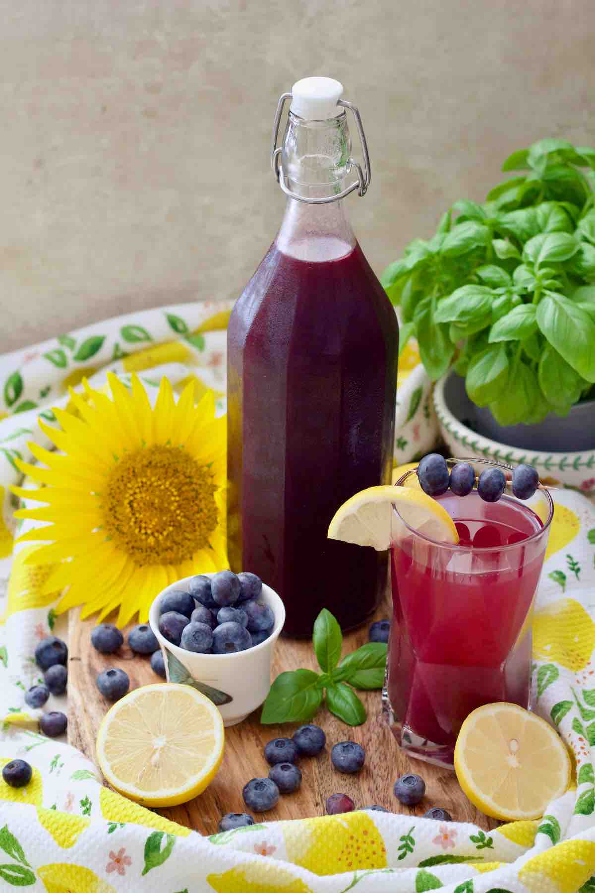 Bottle of blueberry syrup, diluted blueberry drink in a glass, garnishes.