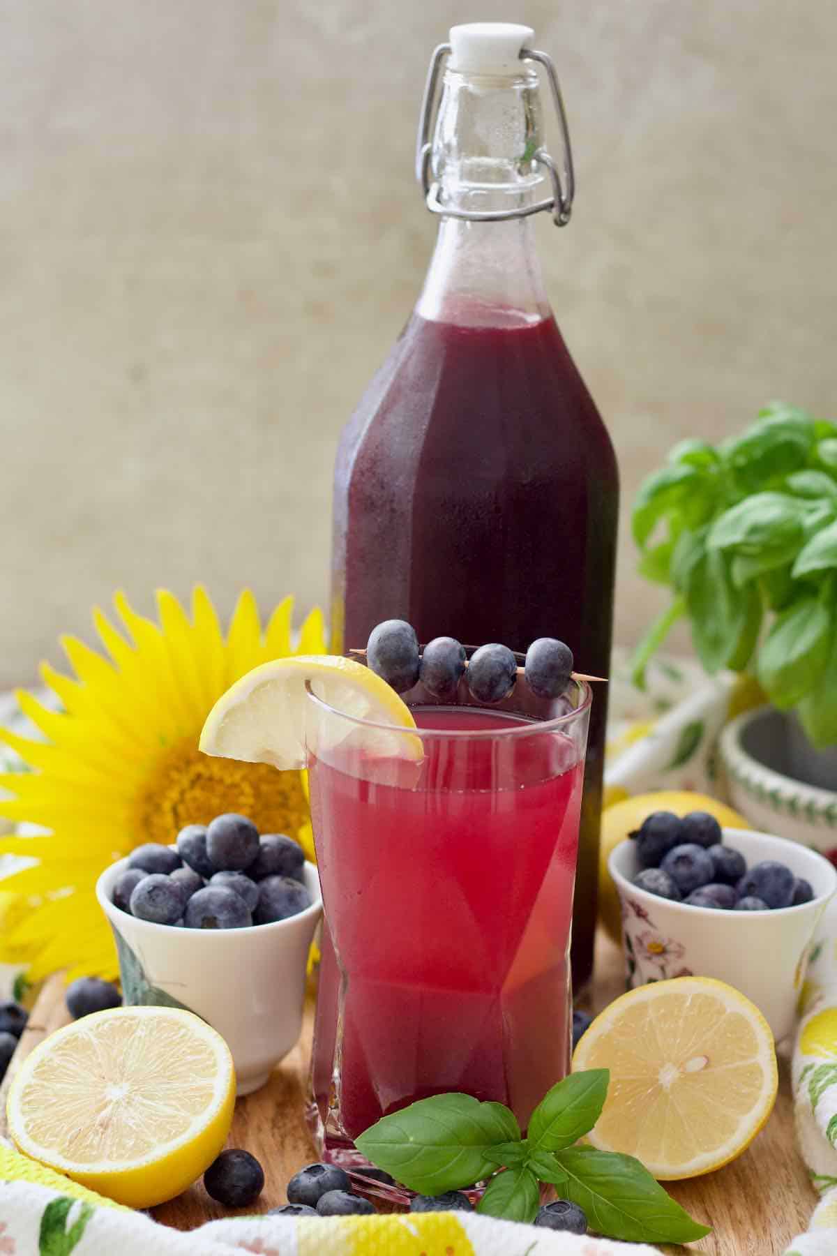 Blueberry syrup in a bottle and some diluted in a glass in front.