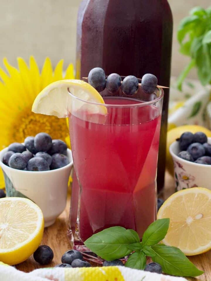 Diluted blueberry cordial drink in a glass garnished with blueberries and lemon.