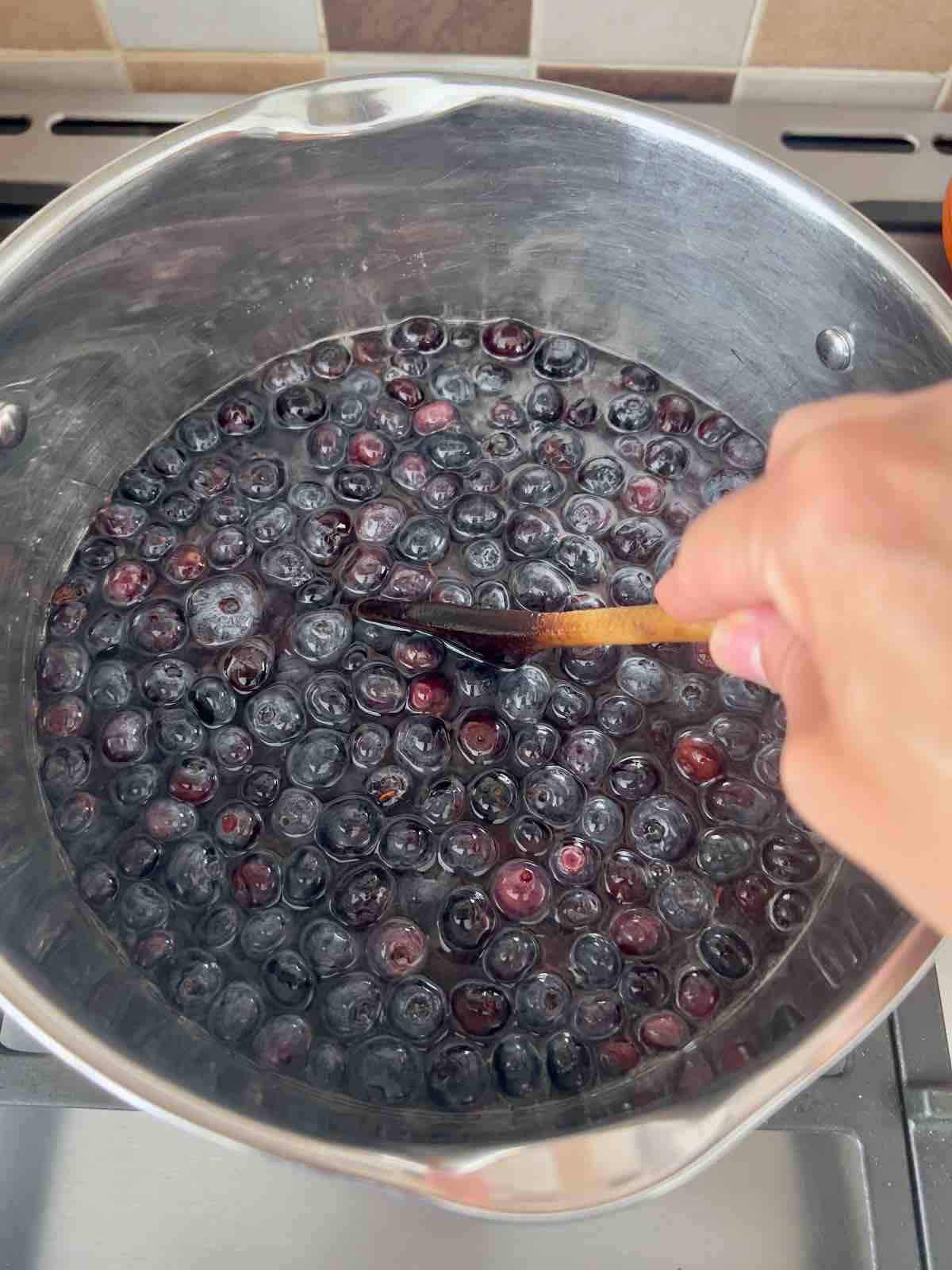 Stirring blueberry, sugar, water, lemon juice mixture with wooden spoon.