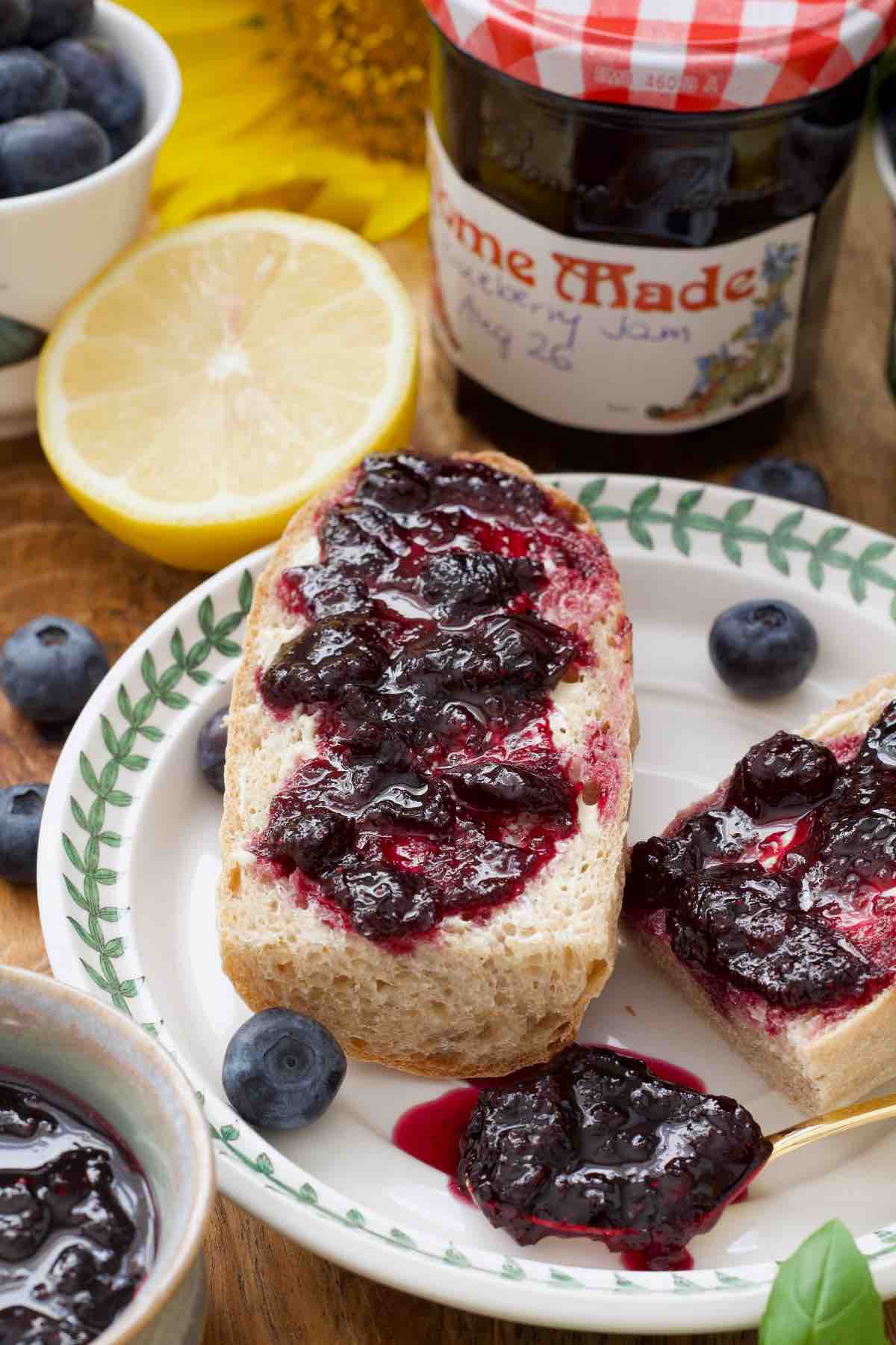 Close up of a piece of baguette topped with blueberry jam and some jam on a spoon.