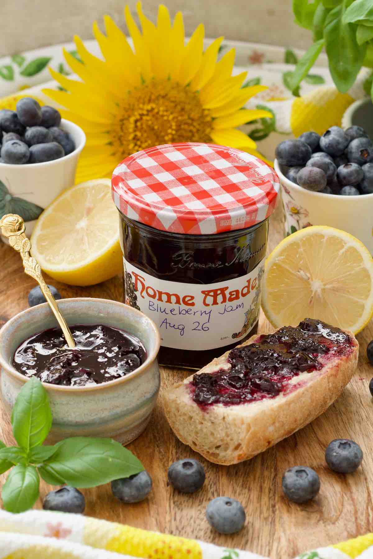 Labelled jar with blueberry jam, jam in a small bowl and a piece of jam topped baguette.