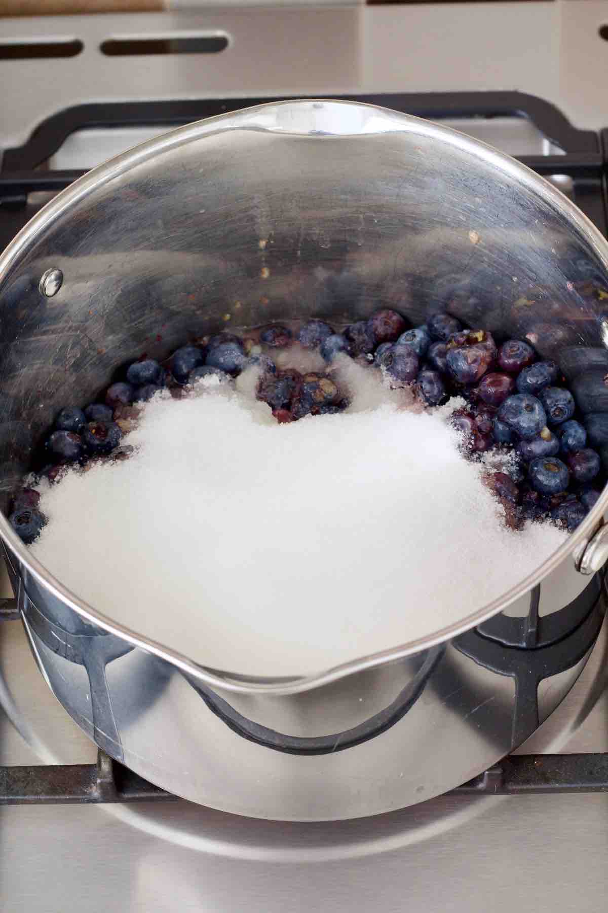 Sugar and lemon juice added to blueberries in a pan.