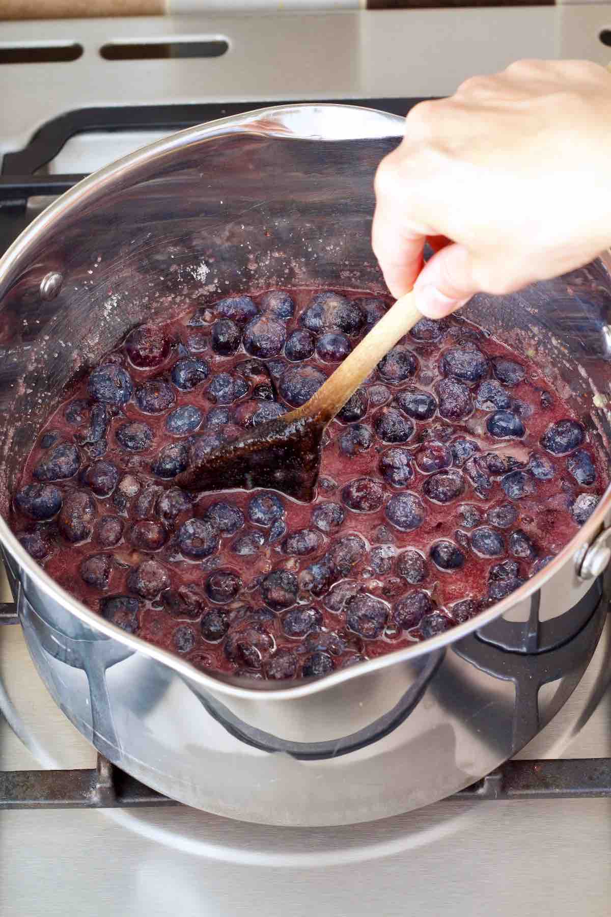 Stirring blueberries, sugar and lemon juice with a wooden spoon.