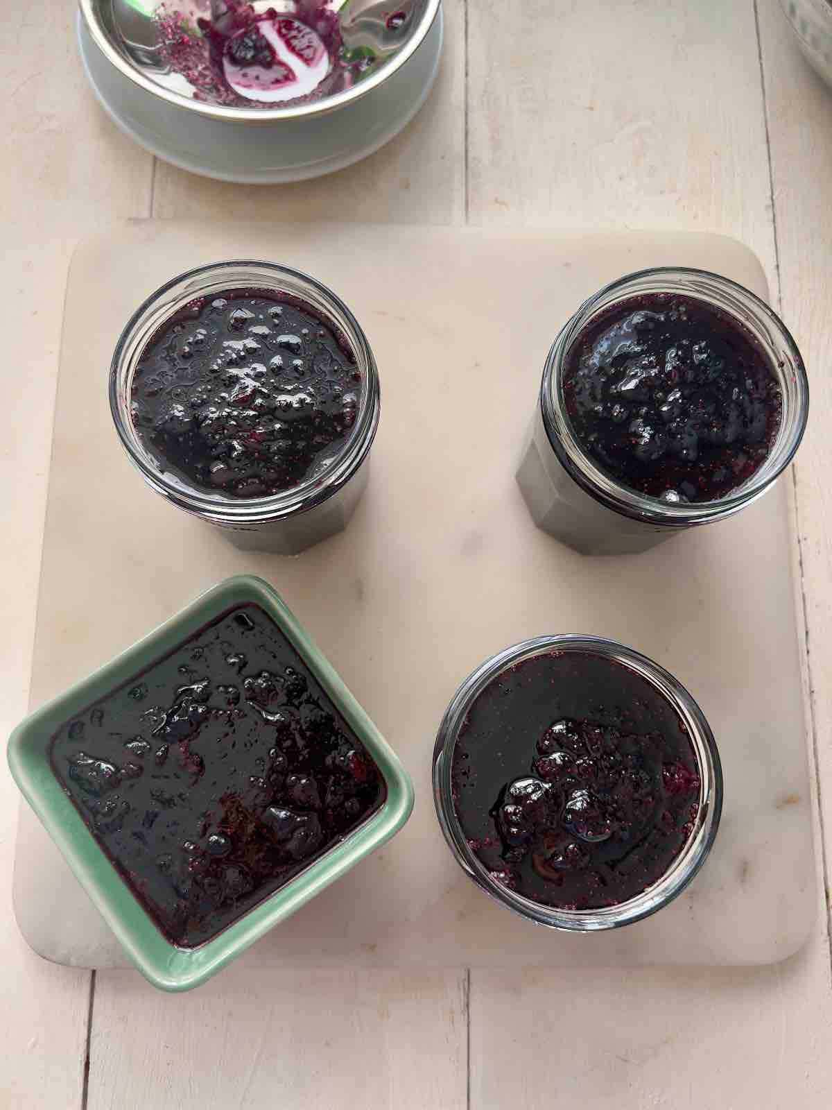 Three open jars and one small bowl with blueberry jam.