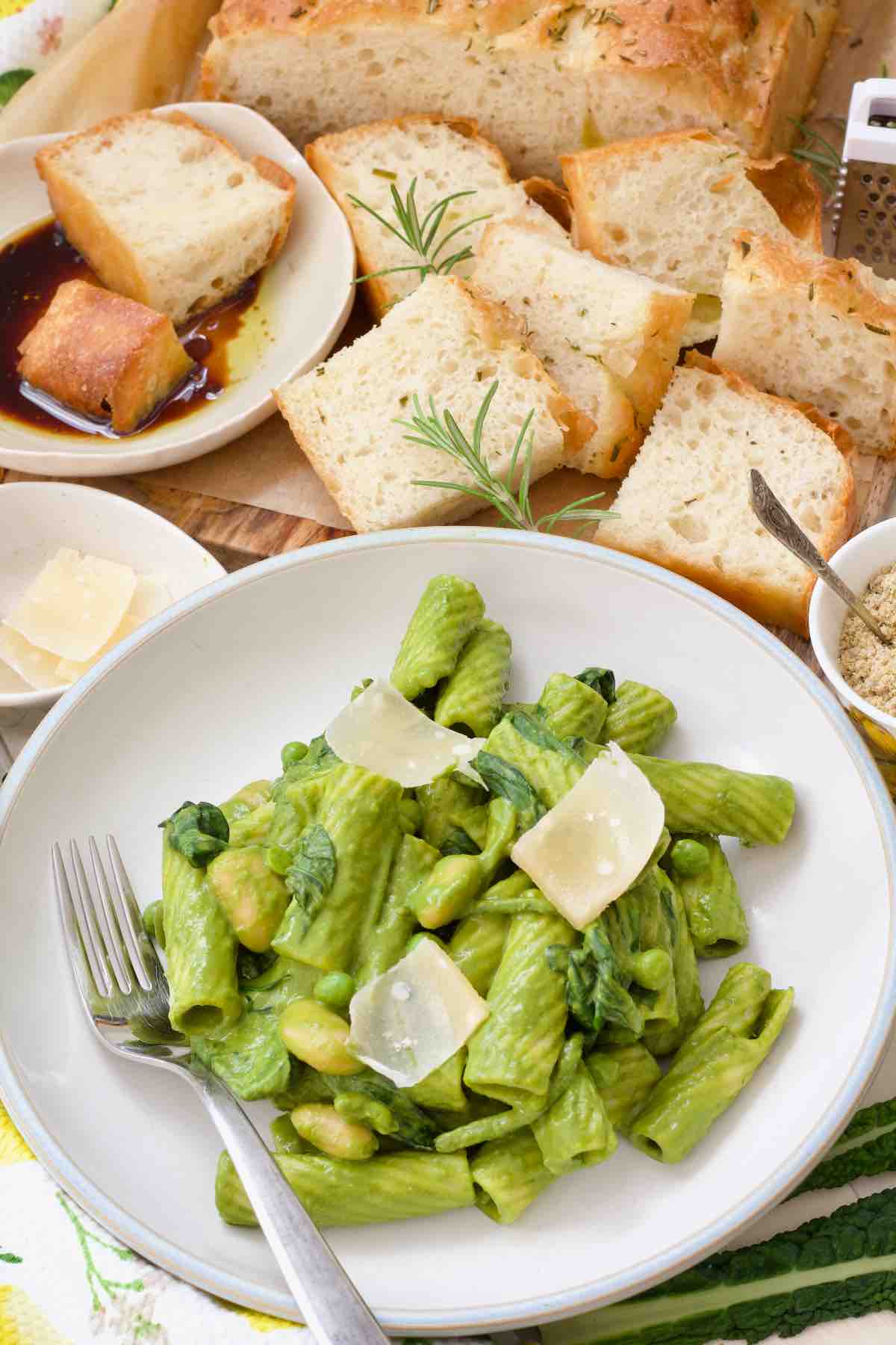 Bowl of green pasta with parmesan shavings and focaccia slices.