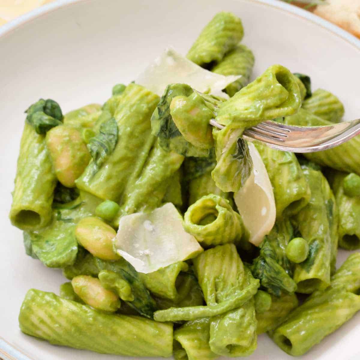 Close up of a bowl of green pasta with a bite ready on the fork.