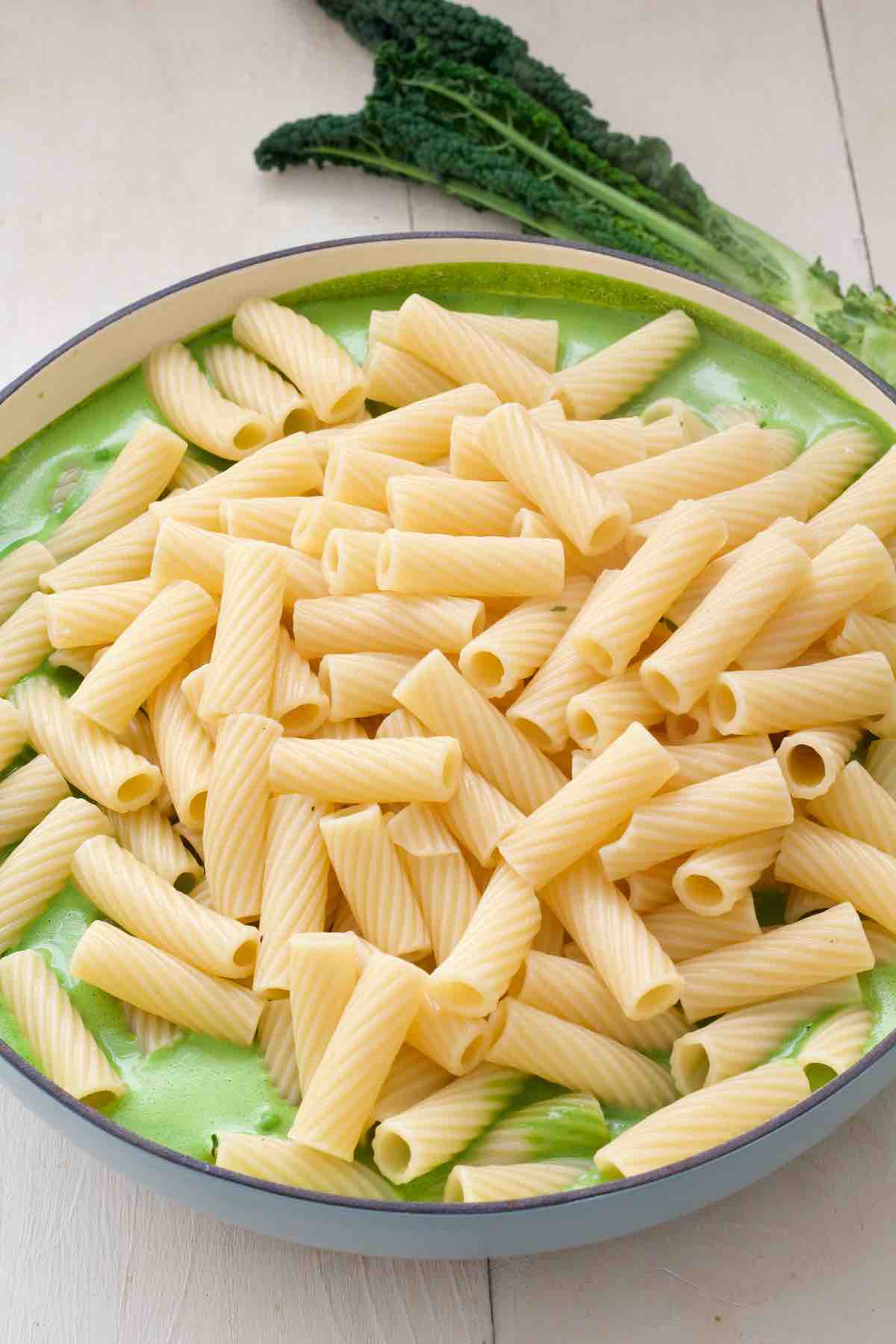 Cooked pasta being added to the green sauce.