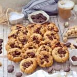 Baked chocolate chip cookies on cooling rack with coffee, and chocolate buttons.