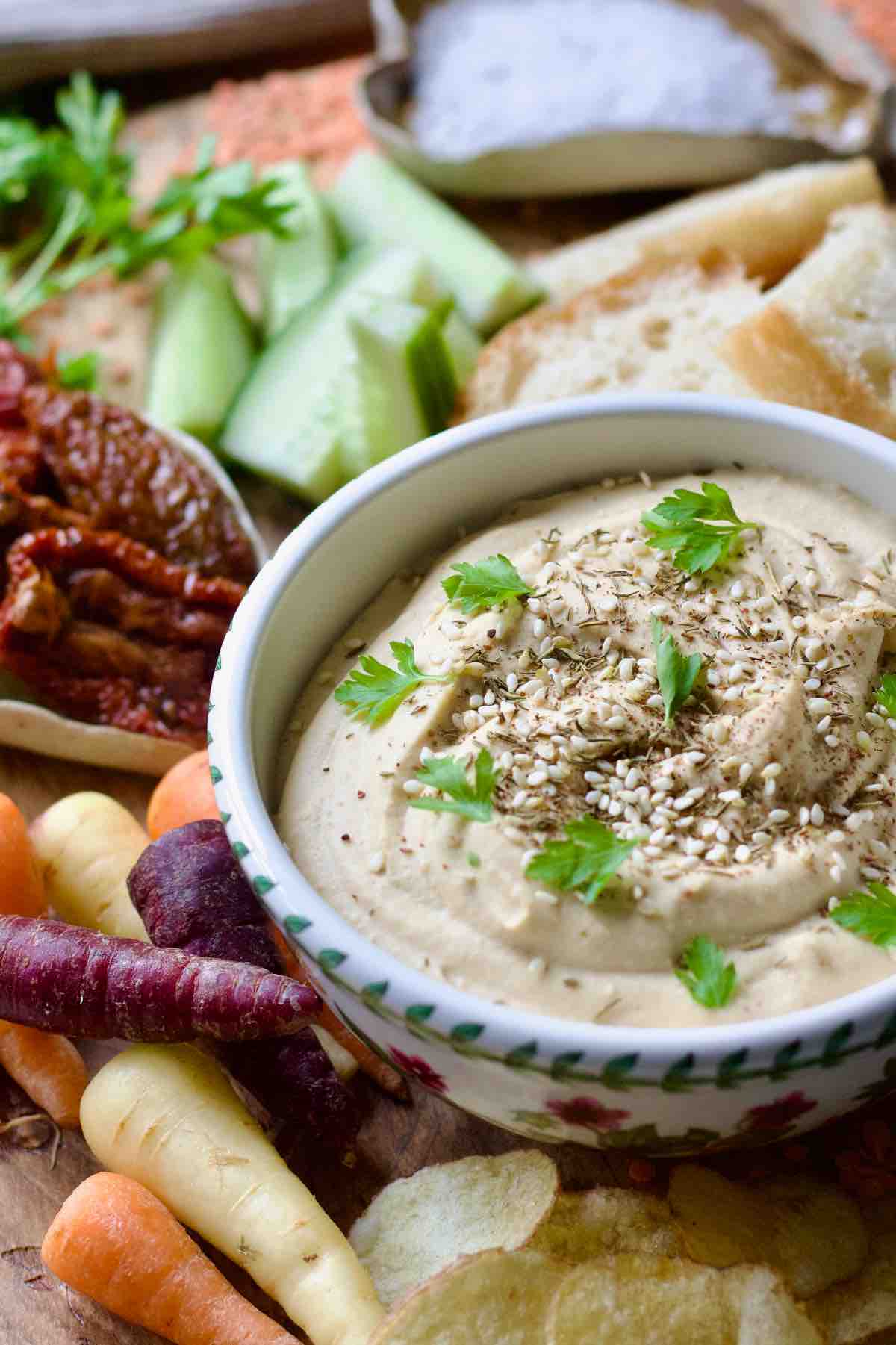 Side view of hummus bowl with carrots and crisps.