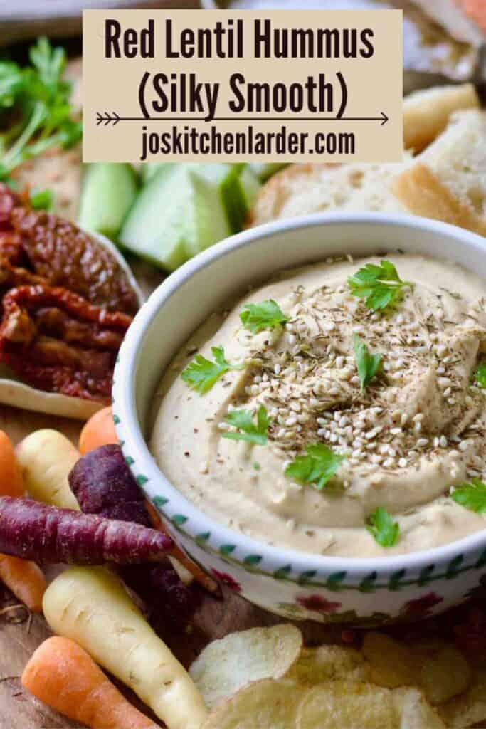 Side view of hummus bowl with carrots and crisps.